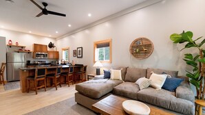 A modern kitchen with a central island, bar stools, a dining area with a sofa, and a ceiling fan. - Pet-Friendly Saugatuck Cottage | Hot Tub • Fire Pit • Dog Park (Saugatuck)