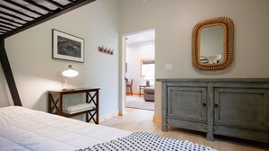 A bedroom with a bed, bedside table, lamp, dresser, mirror, and a hallway leading to another room. - Pet-Friendly Saugatuck Cottage | Hot Tub • Fire Pit • Dog Park (Saugatuck)