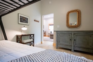 A bedroom with a bed, bedside table, lamp, dresser, mirror, and a hallway leading to another room. - Pet-Friendly Saugatuck Cottage | Hot Tub • Fire Pit • Dog Park (Saugatuck)