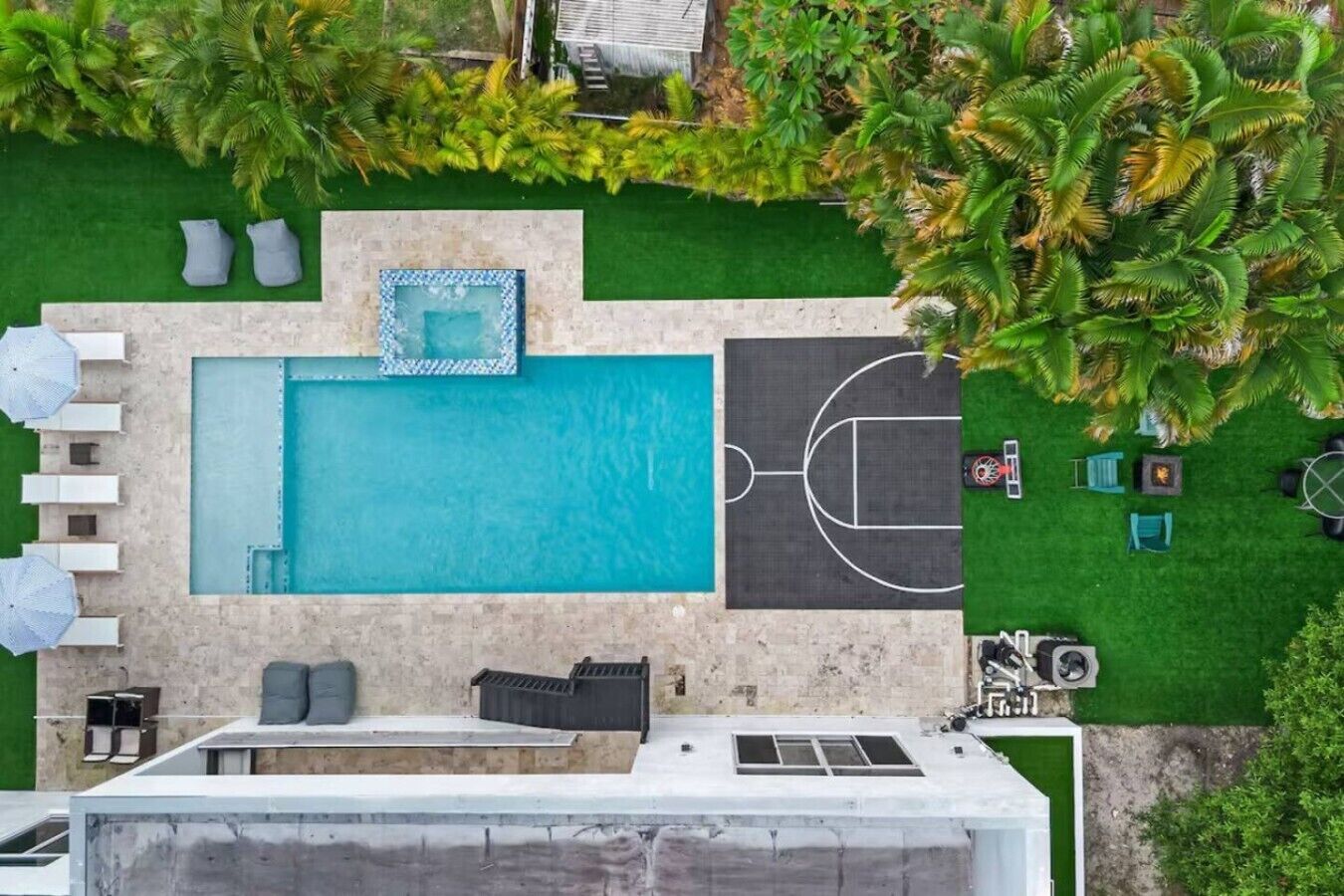 An aerial view of a rooftop pool area with a swimming pool, sun loungers, and a basketball court.