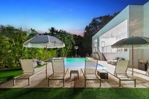 A pool area with lounge chairs and umbrellas, surrounded by greenery and a modern building. - Modern Luxe 2021Built Heated Pool/Jacuzzi/Gameroom (Fort Lauderdale)