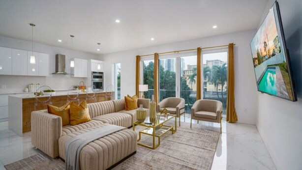 Un salon moderne avec un canapé, des fauteuils, une table basse et une grande fenêtre donnant sur la ville.