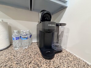 A Keurig coffee maker, a glass carafe, and several bottles of Kirkland water on a granite countertop. - 4BR2BA Creekside Edgewood Retreat Near World Cup (Atlanta)