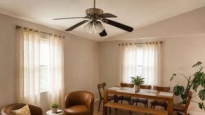 Ein Wohnzimmer mit braunem Ledersessel, einem Holztisch, einem Esstisch mit Stühlen und einem Deckenventilator.