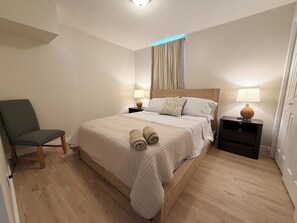 A neatly arranged bedroom with a bed, two bedside tables, a chair, and a lamp. - 4BR2BA Creekside Edgewood Retreat Near World Cup (Atlanta)