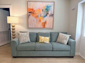 A grey sofa with patterned cushions, a floor lamp, and a colorful abstract painting on the wall. - 4BR2BA Creekside Edgewood Retreat Near World Cup (Atlanta)