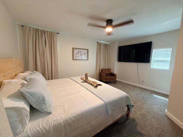 A bedroom with a bed, a ceiling fan, a mounted TV, and a window with blinds.