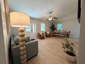 A living room with a sofa, a lamp, a ceiling fan, a dining table, and a potted plant. - 4BR2BA Creekside Edgewood Retreat Near World Cup (Atlanta)