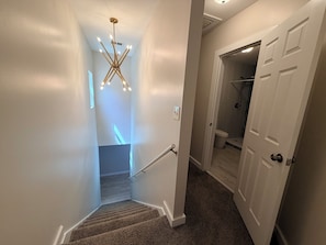 A hallway with a carpeted staircase, a modern chandelier, and a bathroom with a shower and toilet visible. - 4BR2BA Creekside Edgewood Retreat Near World Cup (Atlanta)