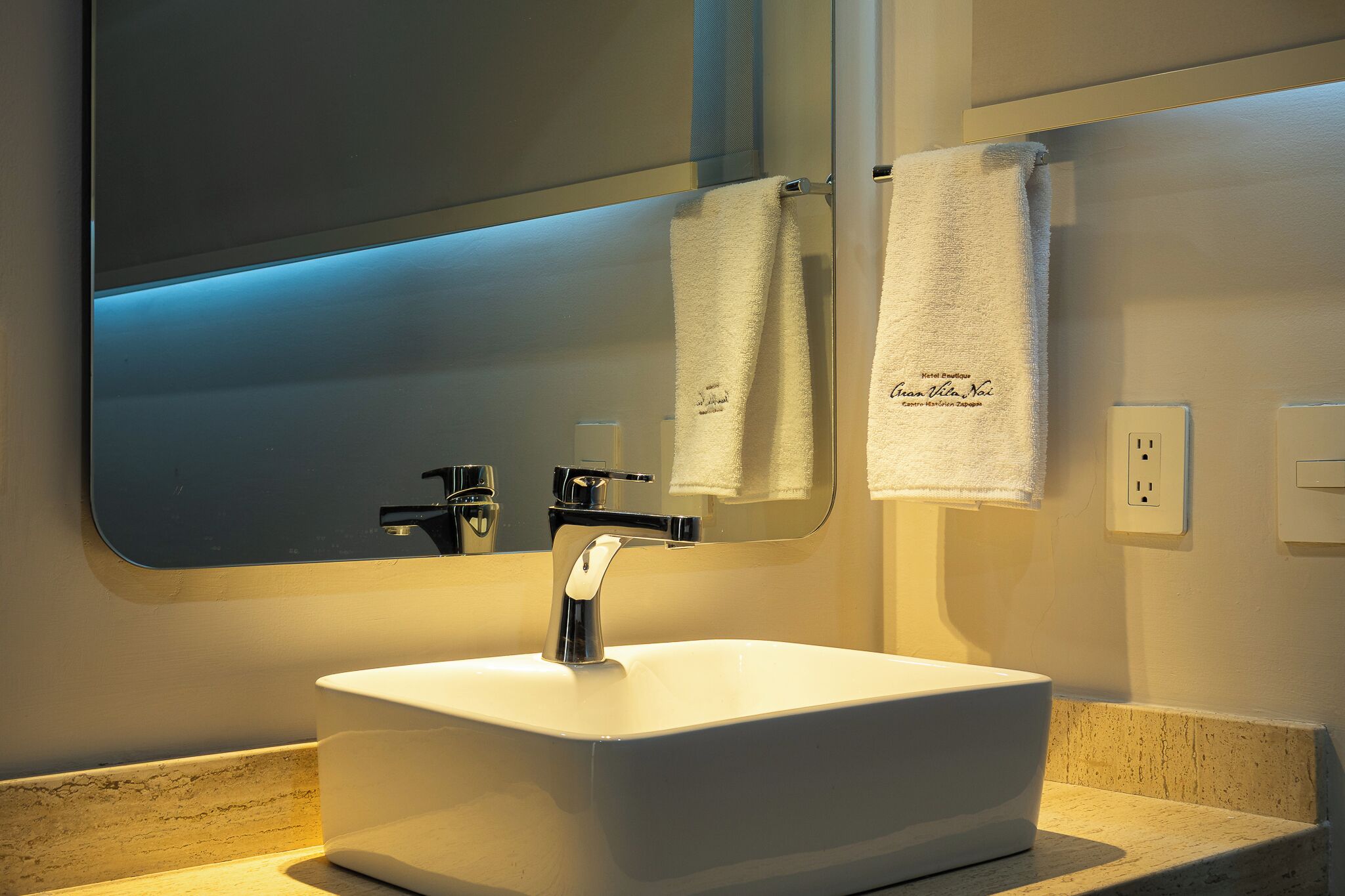 A bathroom with a white sink, a mirror, and two towels hanging on the wall.