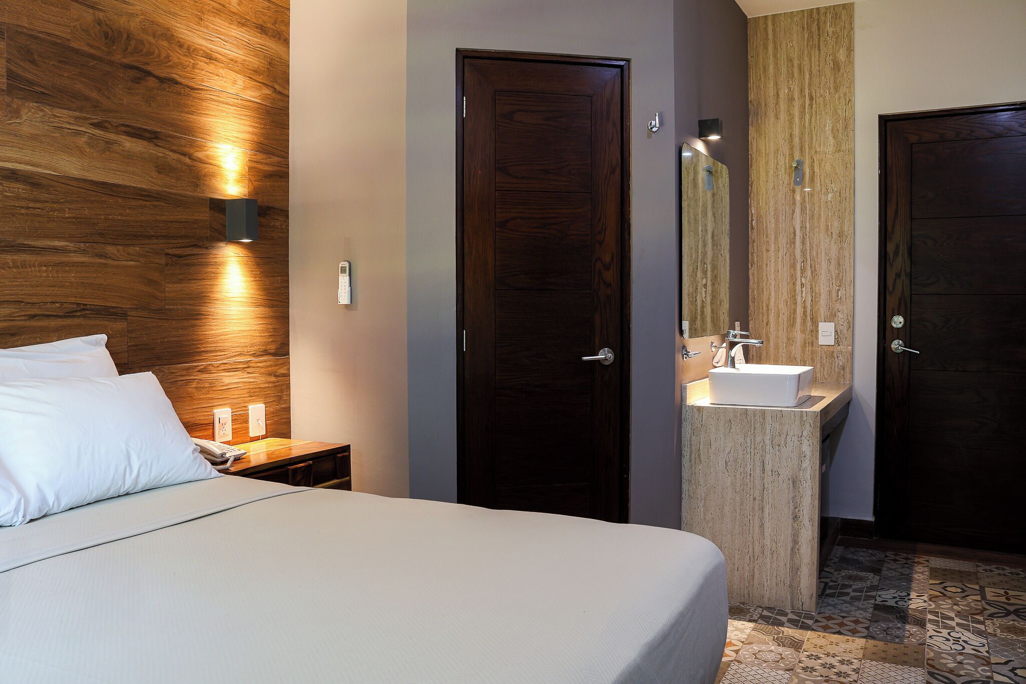 Ein Hotelzimmer mit einem Bett, einem Nachttisch, einem Badezimmer mit Waschbecken und zwei Türen.