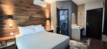 A modern hotel room with a wooden headboard, a bed with white linens, a bedside table, a built-in vanity with a mirror, and a door leading to a bathroom.. Gran Vila Nai Boutique Hotel