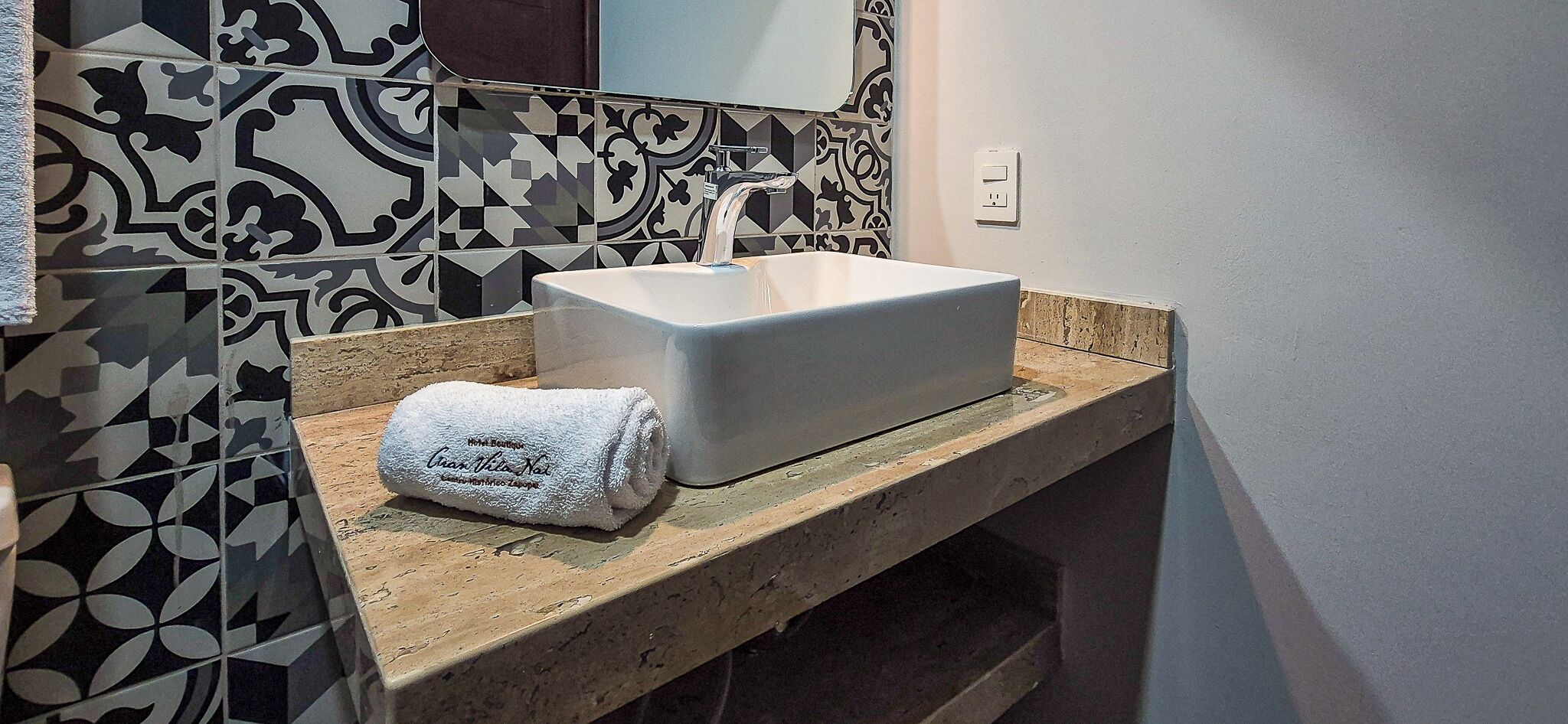 Un baño con un lavamanos blanco, una toalla sobre el mostrador y baldosas estampadas.