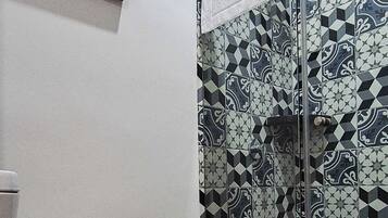 Ein Badezimmer mit Toilette, einer Dusche mit gemusterten Fliesen und einem gerahmten Bild an der Wand.
