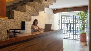 A reception desk with a laptop, a potted plant, and a staircase with stone steps. - Gran Vila Nai Boutique Hotel (Zapopan)