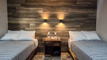 Two single beds with white linens, a wooden nightstand with a lamp, and a wall-mounted light fixture.