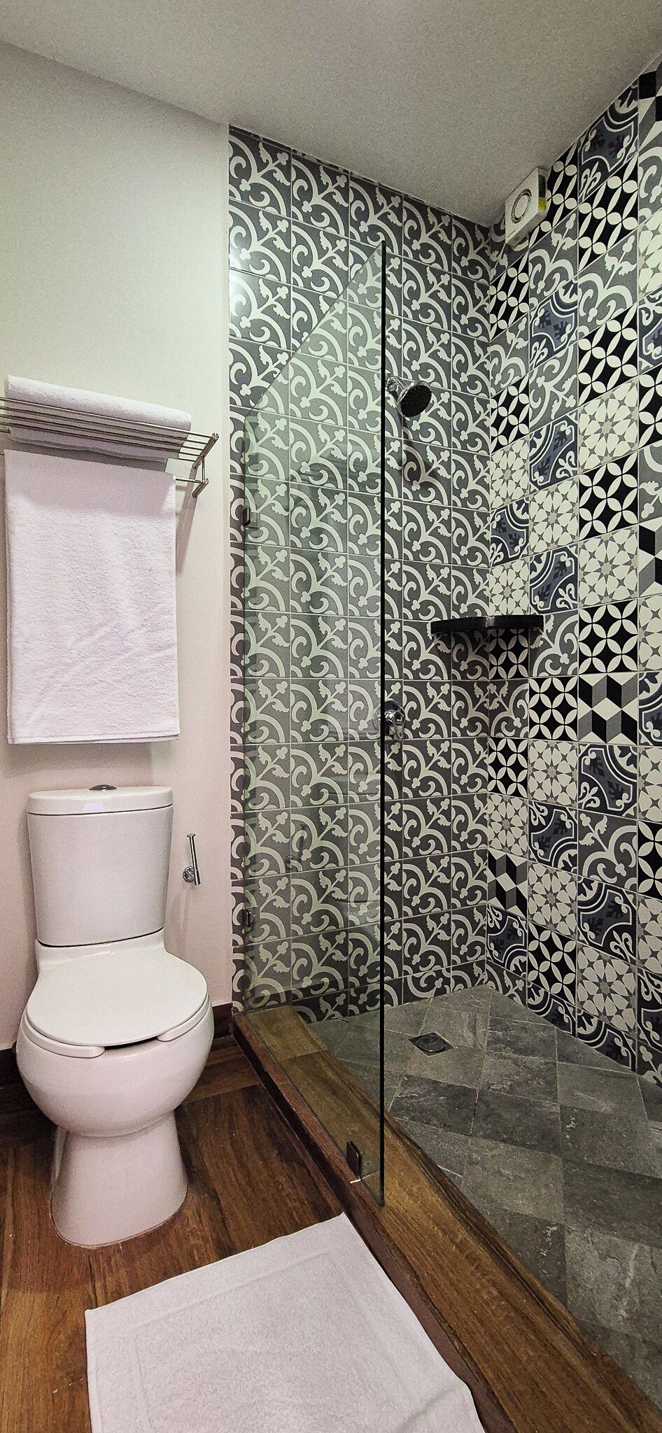 A bathroom with a toilet, a shower with a glass door, and patterned tiles on the walls.
