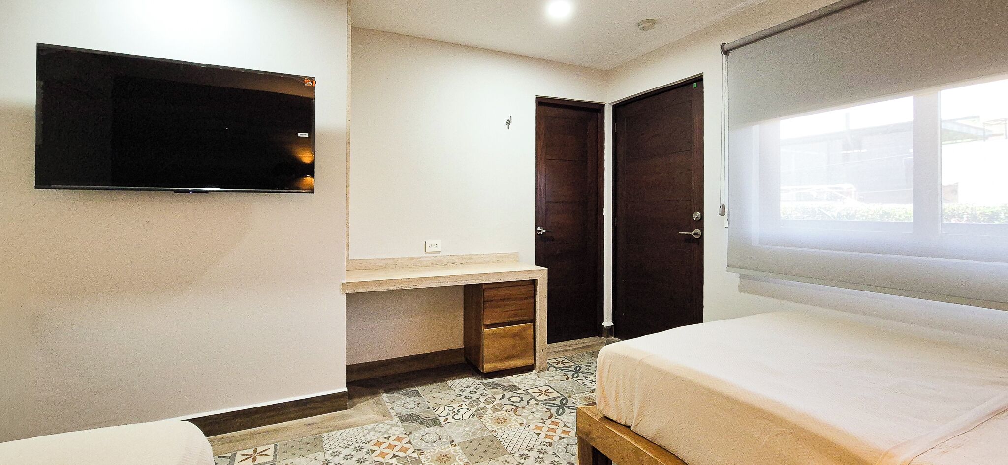 A bedroom with a bed, a desk, a wardrobe, and a TV mounted on the wall.