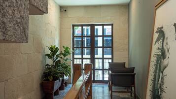 Un pasillo con un banco, plantas en macetas, una puerta con paneles de vidrio y una pared con un mural.