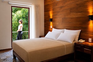 Una habitación de hotel con cama, mesita de noche, teléfono y vistas a zonas verdes.