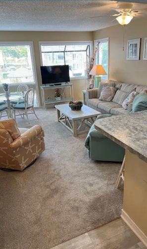 Ein Wohnzimmer mit Fernseher, einer Couch, einem Couchtisch und einem Essbereich mit Stühlen.