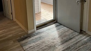 Een kamer met een schuifdeur naar een balkon, een deur met sleutelgat en een klein vloerkleed.