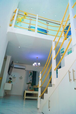 Ein mehrstöckiger Innenraum mit Treppe, einer Deckenleuchte und einem Fernseher.