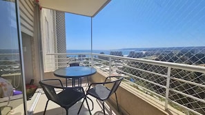 A balcony with a table and chairs, a view of the cityscape, and a clear sky.