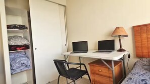 A room with a desk, two laptops, a lamp, a chair, a bed, and a wardrobe.