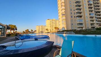 A swimming pool with hot tubs and lounge chairs, surrounded by tall residential buildings.