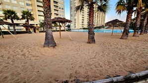 Ein Sandstrand mit Palmen und einem Pool im Hintergrund.