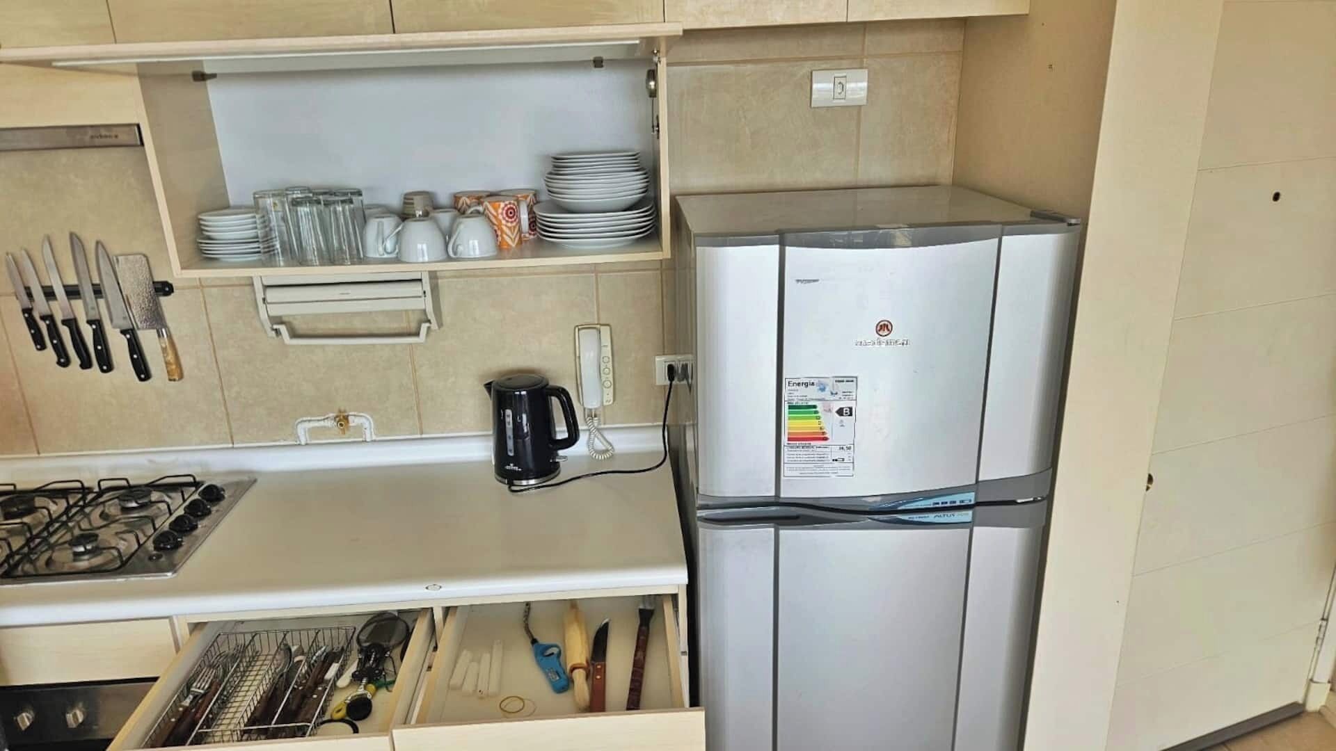 A compact kitchen with a gas stove, a refrigerator, and a drawer with utensils.
