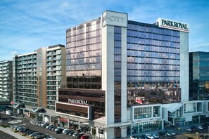 Ein mehrstöckiges Hotel mit einem gut sichtbaren 'PARKROYAL'-Schild, einem Parkplatz und angrenzenden Gebäuden.