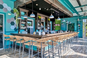 A bar area with a long counter, multiple bar stools, hanging pendant lights, and a wall with hexagonal patterns and greenery. - Mini Mouse House | Mini Golf & NO FEE Waterpark! (Davenport)