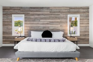 Ein modernes Schlafzimmer mit einer grauen Schlafsofa, einem schwarzen Zierkissen und zwei Nachttischen mit gerahmten Bildern.