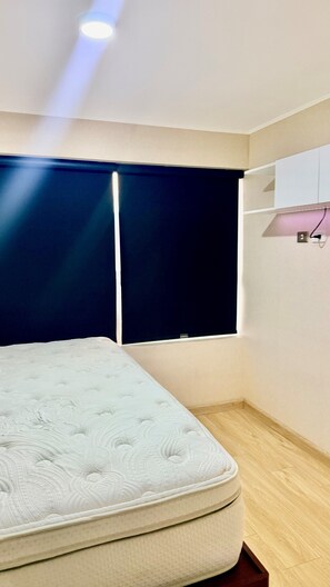 A bedroom with a bed, a dark-colored window blind, a wall-mounted light, and a wooden floor. - "Modern apartment close to San Isidro and San Borja". (La Victoria)