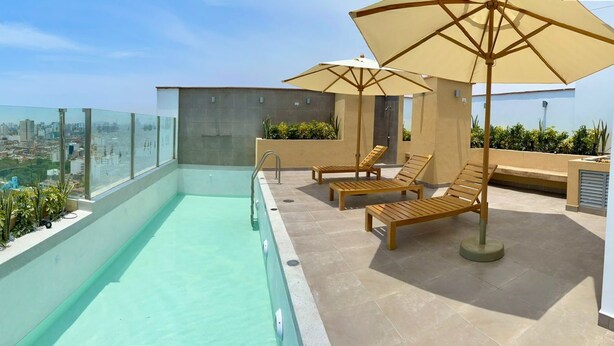 Een dakzwembad met glazen balustrades, houten ligbedden en parasols.