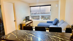 A compact living space with a dining table, a sofa, a TV, and a city view through a large window. - "Modern apartment close to San Isidro and San Borja". (La Victoria)