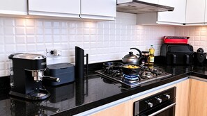 A modern kitchen with a coffee maker, a kettle, a frying pan, and a gas stove.