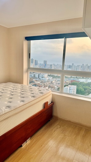 A bedroom with a large window, a bed, and a view of a cityscape.