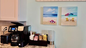 Una cucina con una macchina da caffè, un frullatore e un macinino per caffè. Due quadri alle pareti raffigurano scene di spiaggia.