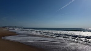 Ein Strand mit Wellen, einem Steg und blauem Himmel.