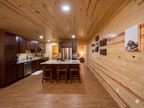 Ein Interieur einer Holzhütte mit einer Küche, die dunklen Schränken, einer Arbeitsplatte aus Granit, Edelstahlgeräten und einer zentralen Kochinsel mit Barhocker ausgestattet ist.