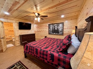 Ein schlafzimmer im Chalet-Stil mit Bett, Deckenventilator, montiertem Fernseher und Wandbild mit Bärenmotiv.
