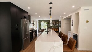 A modern kitchen with a marble island, black cabinets, stainless steel appliances, and a central pendant light. - Epic home base under the chief with unbelievable back yard (Squamish)