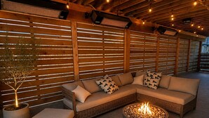 A cozy outdoor seating area with a wicker sofa, a fire pit, and wooden slatted walls. - Epic home base under the chief with unbelievable back yard (Squamish)