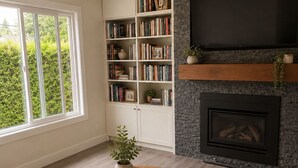 A living room with a sofa, a coffee table with books, a bookshelf, a fireplace, and a TV. - Epic home base under the chief with unbelievable back yard (Squamish)