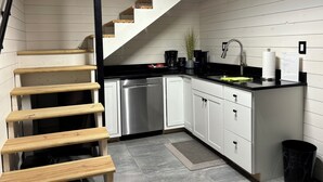 Una cocina con armarios blancos, lavavajillas de acero inoxidable, encimera negra y escalera de madera.