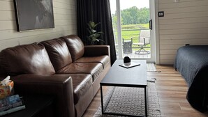 Una habitación con un sofá de cuero marrón, una mesita con un libro, una silla negra y una cama.