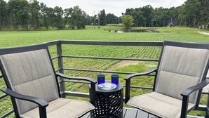 Una terraza con dos sillas y una mesa pequeña, con vista a un campo verde y árboles.